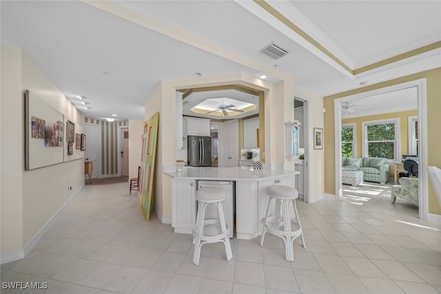 kitchen featuring kitchen peninsula, stainless steel fridge, a tray ceiling, a breakfast bar, and white cabinets