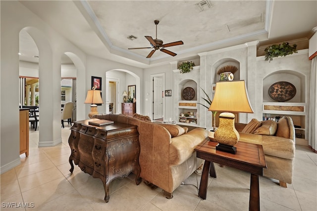 tiled living room featuring ceiling fan, a raised ceiling, ornamental molding, and a fireplace