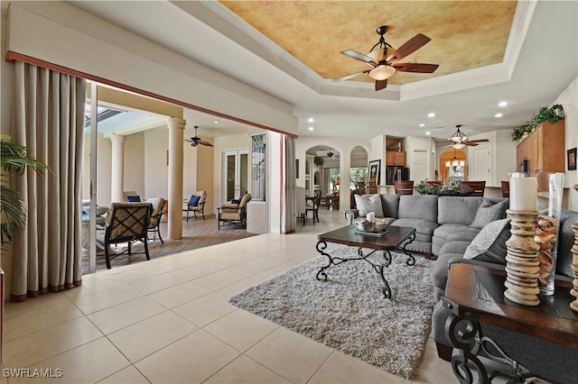 tiled living room featuring ceiling fan, ornate columns, ornamental molding, and a tray ceiling