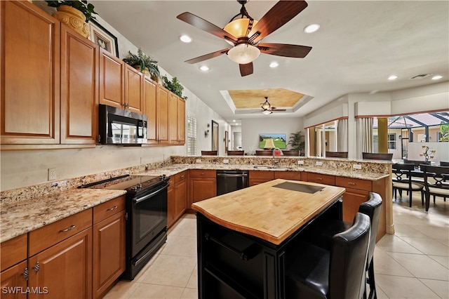 kitchen featuring a center island, a breakfast bar area, sink, a tray ceiling, and black appliances