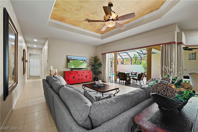 tiled living room with ceiling fan, decorative columns, crown molding, and a tray ceiling