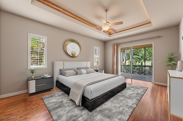 bedroom featuring multiple windows, access to outside, a tray ceiling, and ceiling fan