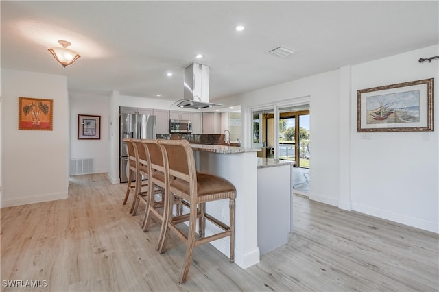 kitchen with light stone countertops, a kitchen breakfast bar, light hardwood / wood-style flooring, island exhaust hood, and appliances with stainless steel finishes