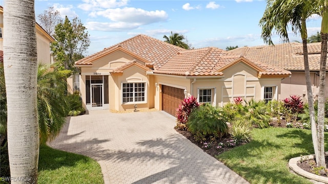 mediterranean / spanish house featuring decorative driveway, a tiled roof, an attached garage, and stucco siding