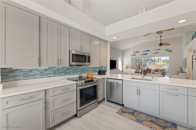 kitchen featuring sink, kitchen peninsula, appliances with stainless steel finishes, ceiling fan, and lofted ceiling