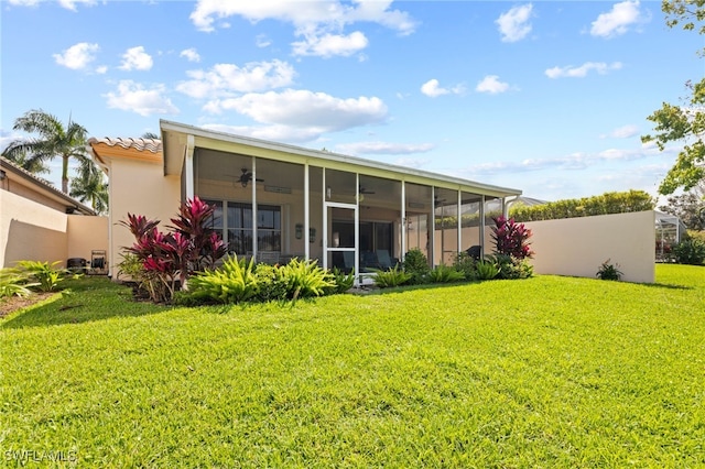 rear view of property with ceiling fan, a sunroom, and a yard