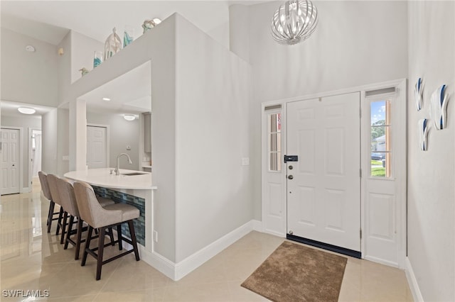 foyer with a towering ceiling, light tile patterned floors, sink, and a notable chandelier