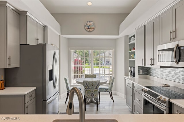 kitchen with stainless steel appliances, light hardwood / wood-style floors, gray cabinetry, and decorative backsplash