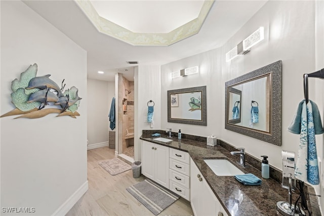 bathroom with vanity, hardwood / wood-style floors, a tile shower, and a raised ceiling