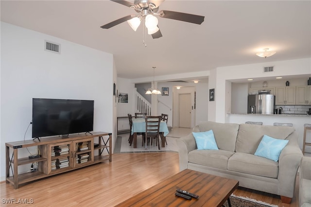 living room featuring ceiling fan with notable chandelier and light wood-type flooring