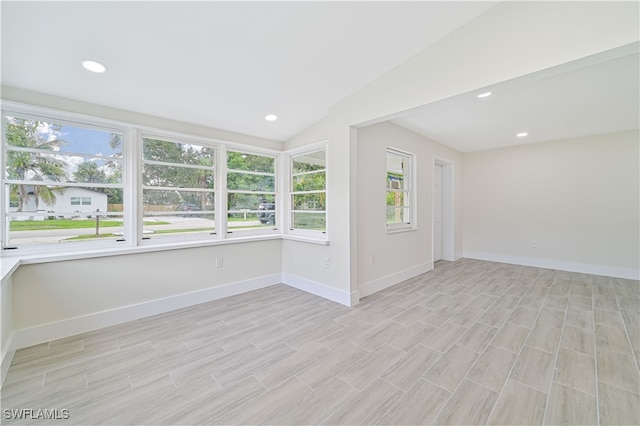 empty room with plenty of natural light, lofted ceiling, and light hardwood / wood-style floors