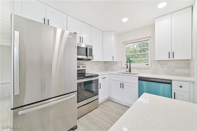 kitchen with stainless steel appliances, white cabinetry, sink, and backsplash