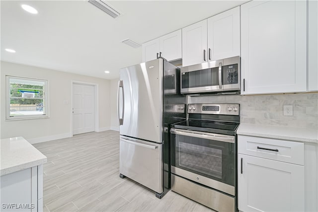 kitchen with stainless steel appliances, white cabinets, light wood-type flooring, and backsplash