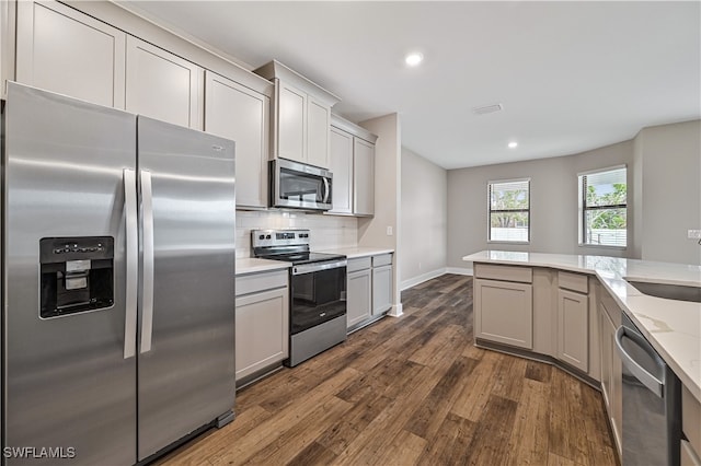 kitchen with decorative backsplash, appliances with stainless steel finishes, light stone countertops, gray cabinetry, and dark hardwood / wood-style flooring