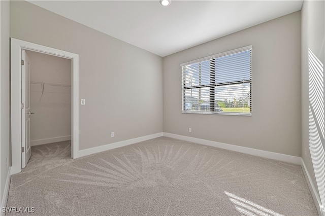 unfurnished bedroom featuring a closet, a walk in closet, and light carpet