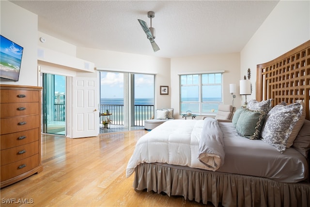 bedroom featuring light wood-type flooring, a textured ceiling, access to outside, ceiling fan, and a water view