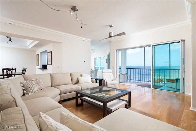 living room with ceiling fan, a textured ceiling, hardwood / wood-style flooring, a water view, and ornamental molding