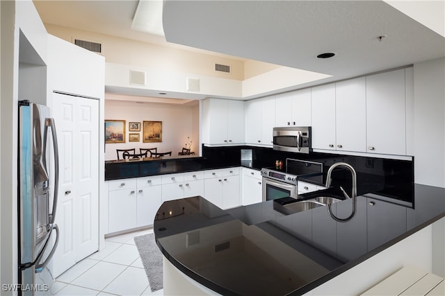 kitchen featuring sink, kitchen peninsula, light tile patterned floors, white cabinetry, and stainless steel appliances