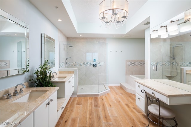 bathroom featuring vanity, a raised ceiling, wood-type flooring, a notable chandelier, and shower with separate bathtub