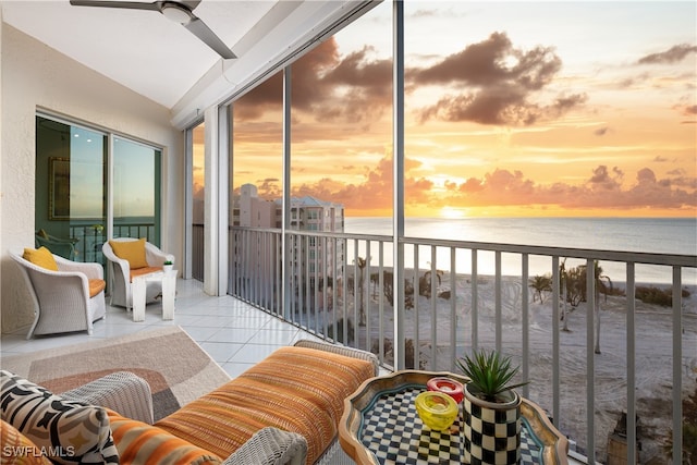 balcony at dusk featuring ceiling fan, a water view, and a beach view