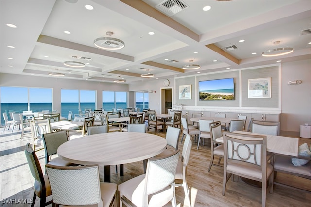 dining space featuring light hardwood / wood-style floors, a water view, beam ceiling, and coffered ceiling