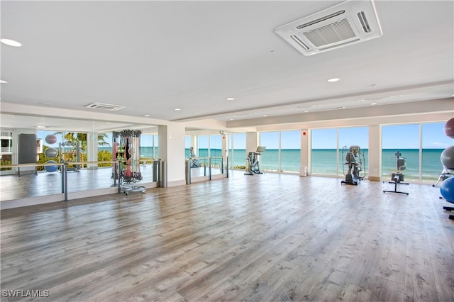 exercise room featuring wood-type flooring, a water view, and plenty of natural light