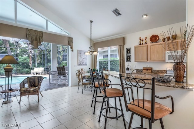 kitchen featuring light brown cabinetry, vaulted ceiling, hanging light fixtures, light tile patterned floors, and dark stone counters