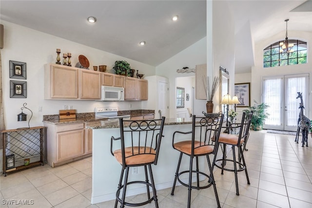 kitchen featuring a kitchen breakfast bar, dark stone counters, light tile patterned floors, light brown cabinets, and white appliances