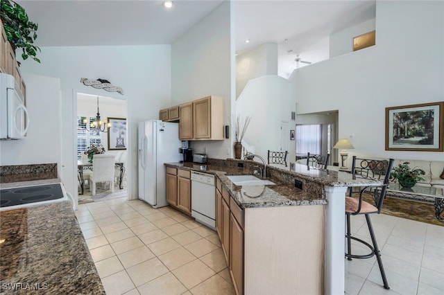 kitchen featuring sink, white appliances, a breakfast bar, dark stone countertops, and light tile patterned flooring