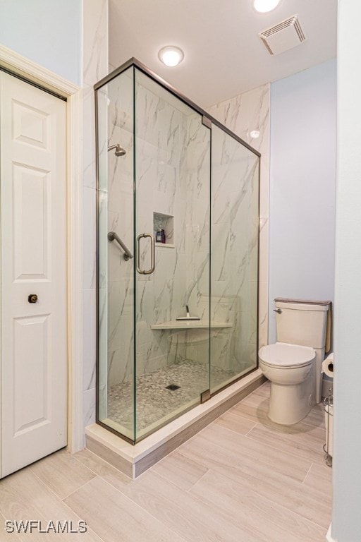 bathroom featuring toilet, an enclosed shower, and wood-type flooring