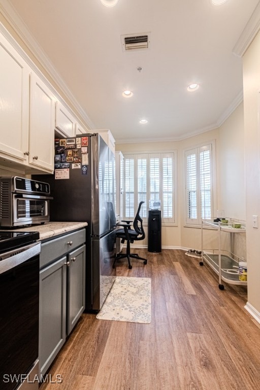 kitchen with light wood-type flooring, stainless steel range oven, ornamental molding, and white cabinets