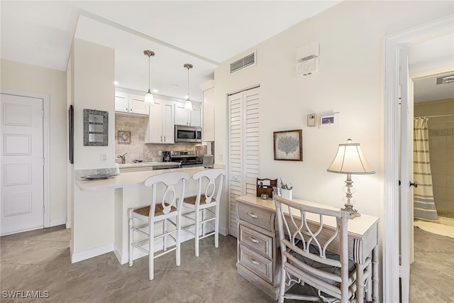 kitchen with kitchen peninsula, appliances with stainless steel finishes, decorative light fixtures, white cabinets, and a breakfast bar area