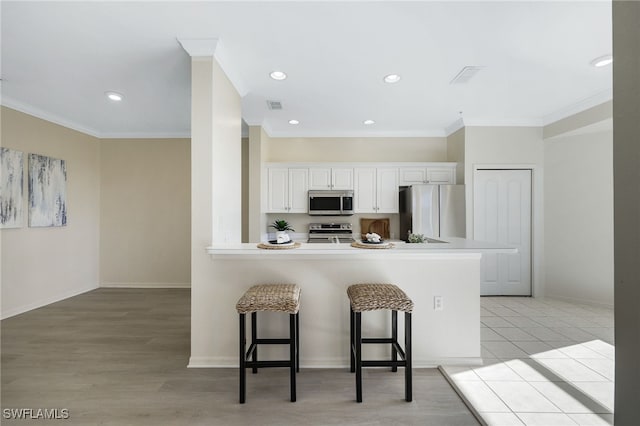 kitchen featuring a kitchen breakfast bar, crown molding, light wood-type flooring, appliances with stainless steel finishes, and white cabinetry