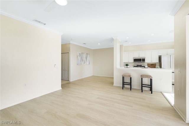 kitchen with crown molding, a breakfast bar, light wood-style flooring, white cabinets, and stainless steel appliances