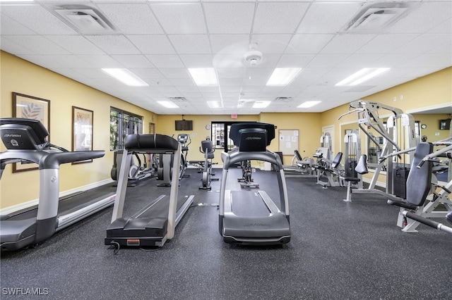 exercise room featuring visible vents, a paneled ceiling, and baseboards