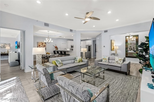 living room with a tray ceiling, ornamental molding, ceiling fan with notable chandelier, and light wood-type flooring