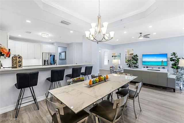 dining area with ceiling fan with notable chandelier, a raised ceiling, sink, ornamental molding, and light hardwood / wood-style floors