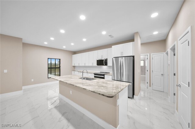 kitchen featuring stainless steel appliances, sink, light stone countertops, an island with sink, and white cabinets