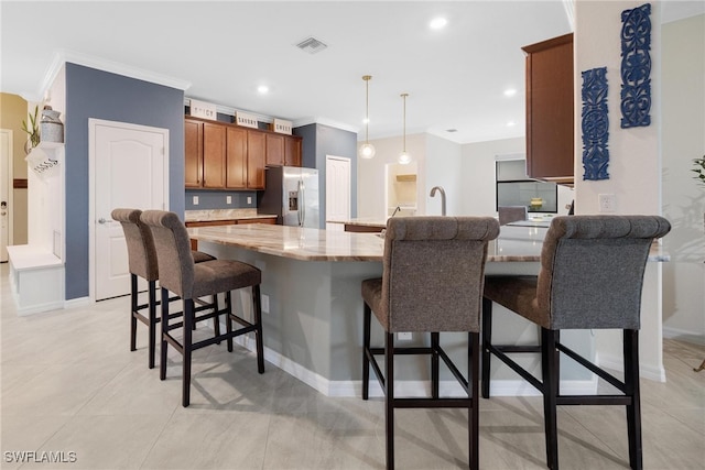 kitchen with a breakfast bar, light stone counters, crown molding, stainless steel fridge, and pendant lighting