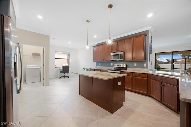 kitchen with sink, appliances with stainless steel finishes, washer / clothes dryer, a kitchen island, and pendant lighting