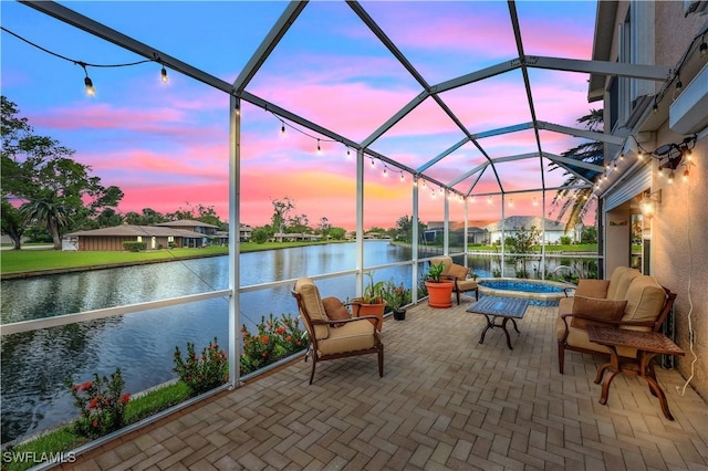 patio terrace at dusk featuring glass enclosure, a water view, and a jacuzzi