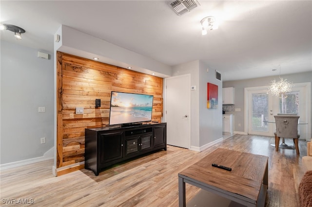 living room with light hardwood / wood-style floors, a chandelier, and wooden walls