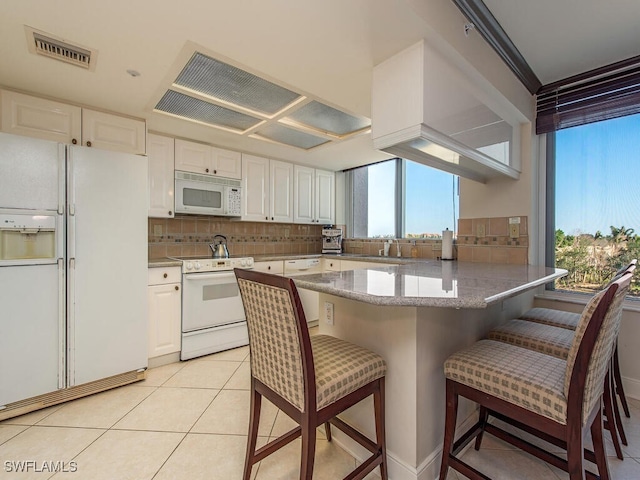 kitchen with white appliances, backsplash, white cabinets, light tile patterned floors, and a kitchen bar