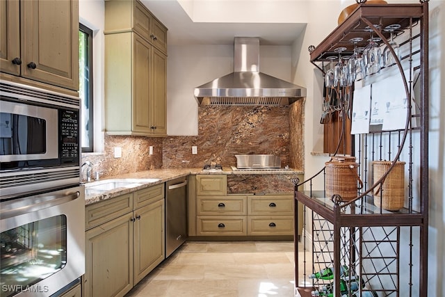 kitchen featuring wall chimney range hood, sink, appliances with stainless steel finishes, tasteful backsplash, and light stone counters