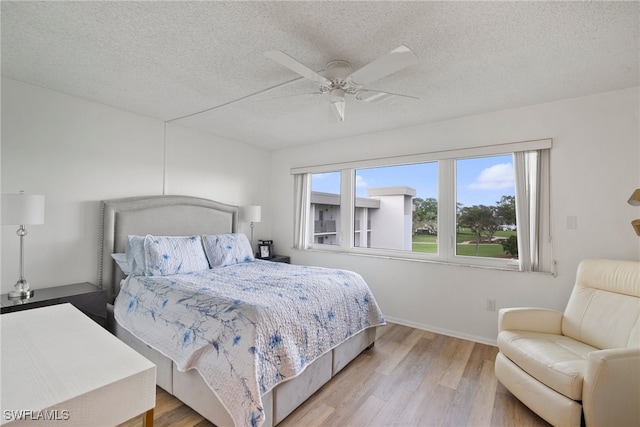 bedroom with a textured ceiling, ceiling fan, and light hardwood / wood-style flooring