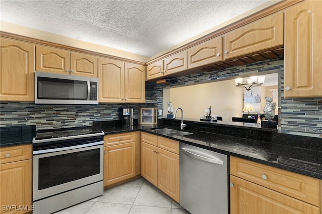 kitchen with appliances with stainless steel finishes, dark stone counters, sink, light tile patterned floors, and an inviting chandelier