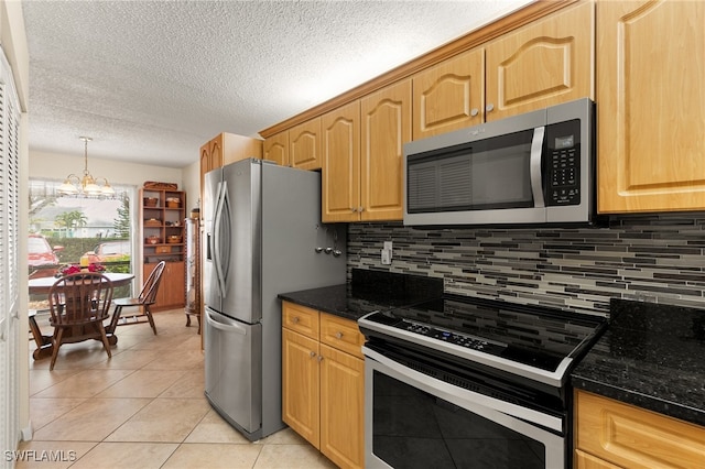 kitchen featuring backsplash, dark stone counters, appliances with stainless steel finishes, light tile patterned flooring, and a chandelier