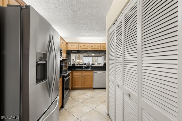 kitchen with light brown cabinets, sink, a textured ceiling, light tile patterned flooring, and appliances with stainless steel finishes