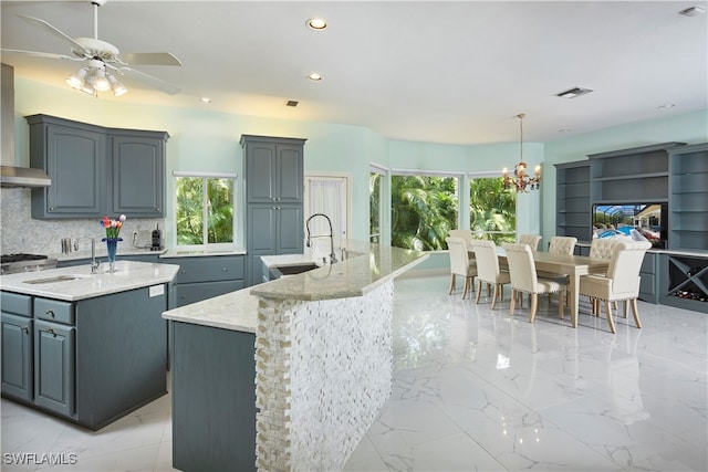 kitchen with an island with sink, decorative backsplash, sink, decorative light fixtures, and ceiling fan with notable chandelier