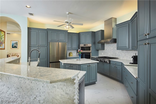 kitchen with sink, wall chimney exhaust hood, tasteful backsplash, a kitchen island with sink, and appliances with stainless steel finishes